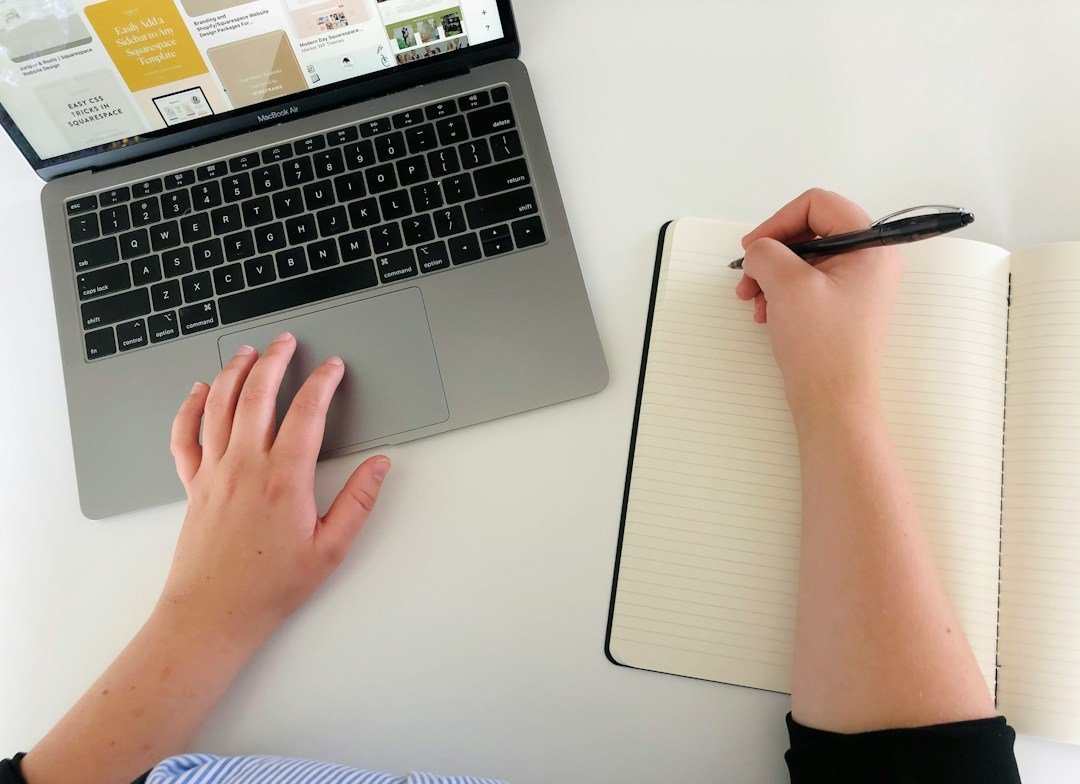 Hands using a laptop and writing notes in a notebook while reviewing a draft